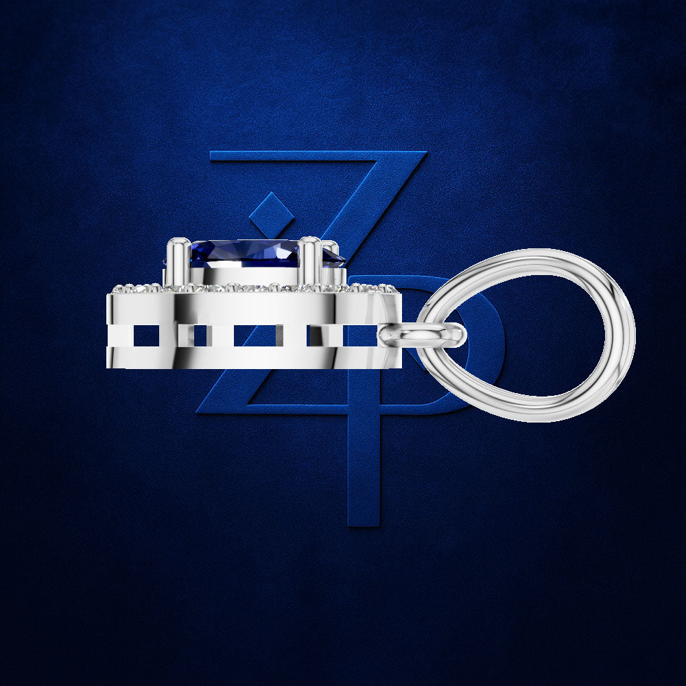 A silver-toned keychain featuring a rectangular bezel-set blue gemstone and a thick coiled ring, displayed against a textured dark blue background with a subtle stylized 'ZP' logo.