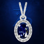 A silver oval pendant necklace featuring a deep blue sapphire center stone surrounded by a halo of small clear stones, set against a dark blue textured background.