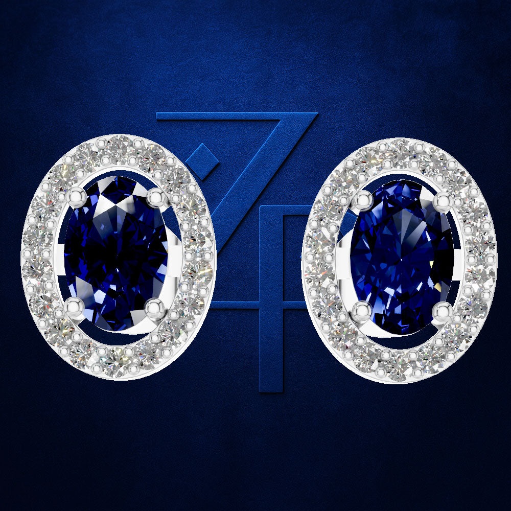 A pair of oval stud earrings with deep blue oval-cut center stones surrounded by a halo of small clear stones, shown on a dark blue background with a faint stylized ZH mark.