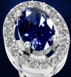 A close-up studio shot of a ring featuring a large oval deep blue sapphire center stone surrounded by a halo of small clear round diamonds in a silver-toned setting, against a dark blue background.