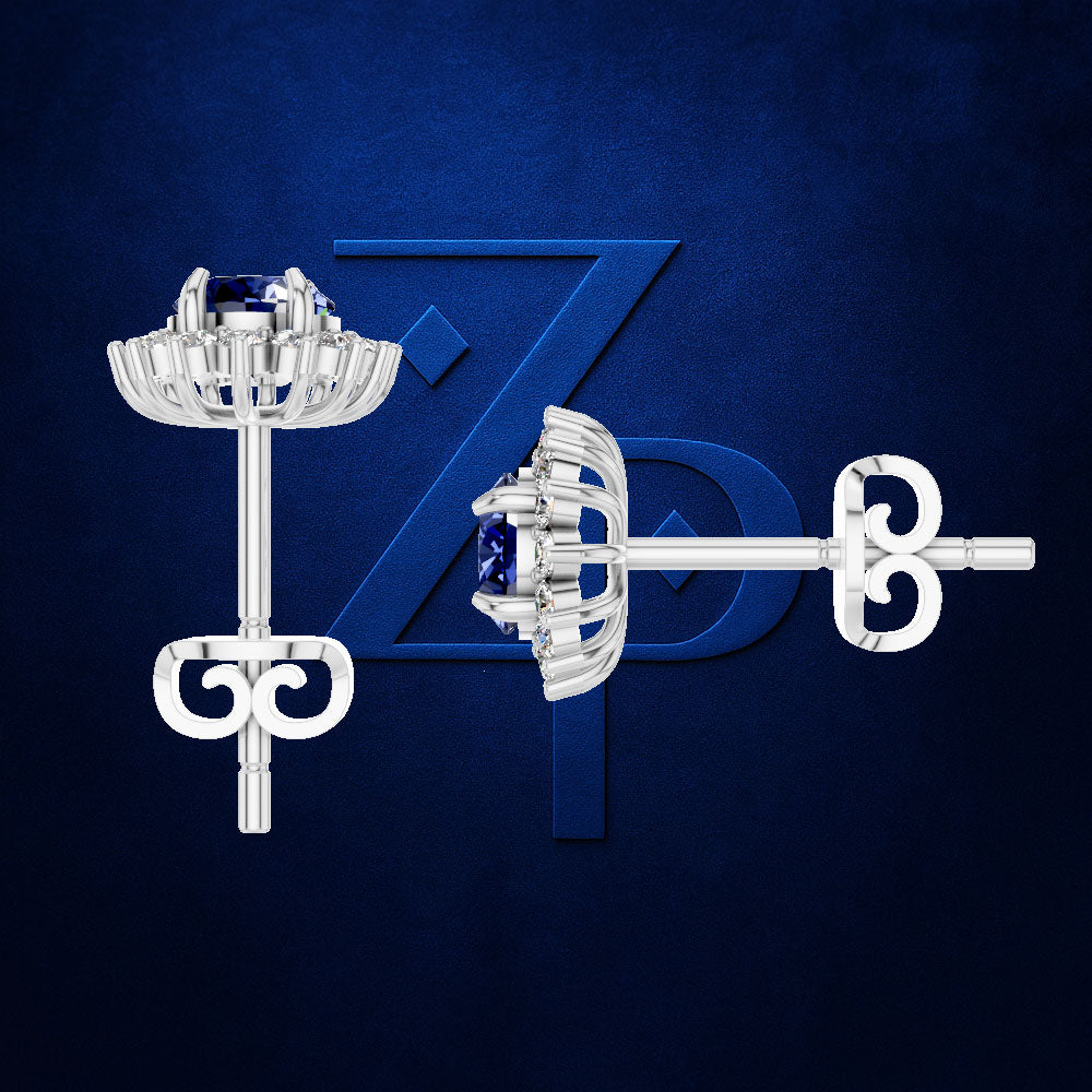 A pair of silver-toned floral stud earrings with deep blue gemstones, shown from both front and side angles against a textured dark blue background with a subtle stylized 'Z' logo.