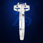 A silver-toned diamond ring with a round-cut blue sapphire center stone, shown in a side profile view against a textured dark blue background.