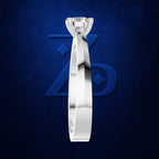 A polished silver-toned solitaire engagement ring with a round brilliant-cut diamond, shown vertically against a textured dark blue background with a subtle stylized logo.