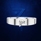 A silver-toned band ring with a single round clear gemstone in a prong setting, centered against a dark blue textured background with a large stylized blue number 7 behind it.