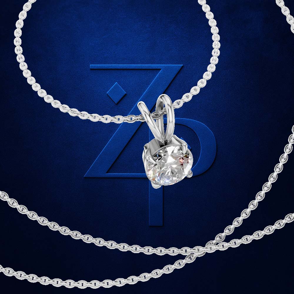 A silver-tone solitaire necklace with a clear round-cut gemstone pendant, draped elegantly on a dark blue textured background with a stylized blue 'ZP' logo behind it.