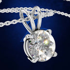 A silver-toned solitaire pendant necklace featuring a large, round brilliant-cut clear gemstone in a prong setting, suspended from a matching chain against a dark blue textured background.