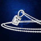 A silver-toned pendant necklace with a clear faceted gemstone in a bezel setting, shown with a matching chain on a dark blue textured background.