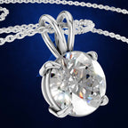 A silver-toned solitaire pendant necklace featuring a large, round brilliant-cut clear gemstone in a prong setting, suspended from a matching chain against a dark blue background.