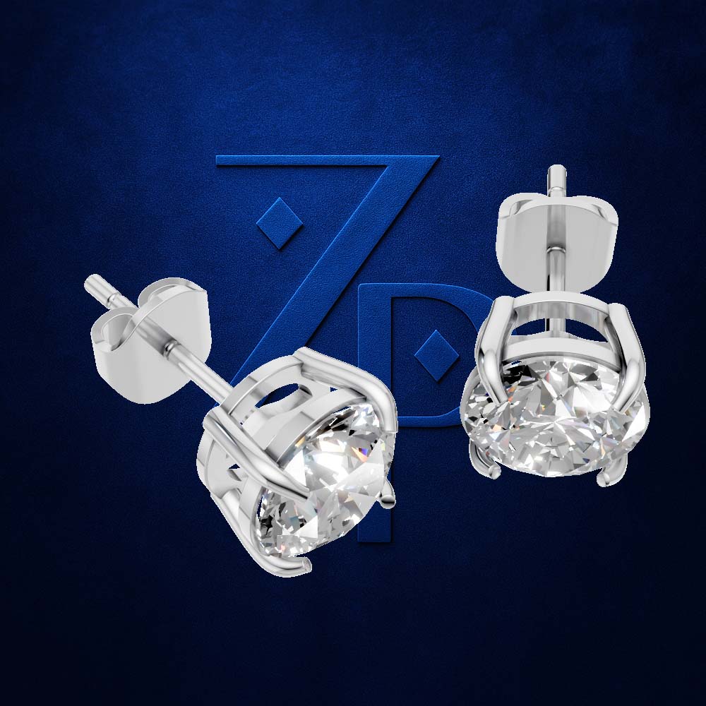 A pair of silver stud earrings with round clear gemstones in a prong setting, shown on a dark blue textured background with a faint stylized 'ZP' logo.