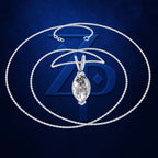 A silver-tone chain necklace with a teardrop-shaped clear gemstone pendant, displayed against a dark blue textured background with a large stylized blue ZP logo behind it.