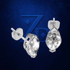 A pair of silver stud earrings with teardrop-shaped clear gemstones, shown from front and side angles against a textured dark blue background with a subtle stylized 'ZP' logo.