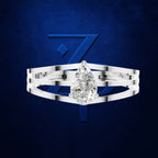A silver-toned ring with a pear-cut clear gemstone, shown against a dark blue textured background with a large stylized blue number 7 behind it.
