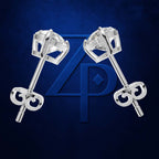 A pair of silver-toned stud earrings with geometric clear gemstone settings and bow-shaped backings, displayed on a dark blue textured background with a large blue monogram logo behind them.
