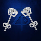 A pair of silver-toned stud earrings with clear gemstones and decorative key-shaped backings, displayed on a dark blue textured background with a large blue monogram behind them.