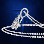 A silver-toned pendant necklace with a large faceted clear gemstone in a bezel setting, shown with a matching chain on a dark blue background with a subtle logo behind it.