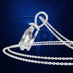 A silver-toned pendant necklace with a faceted clear crystal and a matching chain, arranged on a dark blue textured background with a large stylized blue letter P behind it.