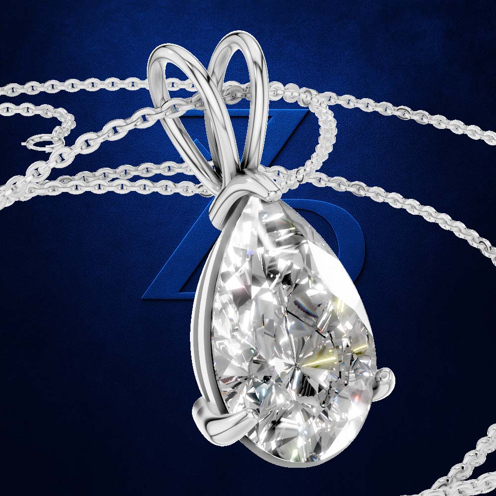 A teardrop-shaped diamond pendant in a polished silver setting, suspended from a matching silver chain against a dark blue background with a subtle geometric logo.