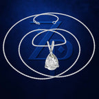 A silver-tone necklace with a teardrop-shaped clear gemstone pendant, displayed against a dark blue textured background with a large stylized 'ZD' logo behind it.
