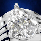 A close-up studio shot of a pear-cut diamond ring set in a polished silver-toned band, with the diamond centered against a deep blue background.