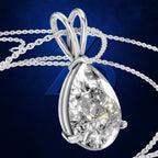 A teardrop-shaped diamond pendant in a silver-colored setting on a matching chain, set against a dark blue background with a subtle geometric design.