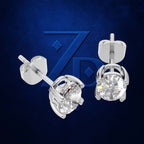 A pair of silver stud earrings with round clear gemstones, shown from both front and side angles against a dark blue textured background with a subtle stylized 'ZP' logo.