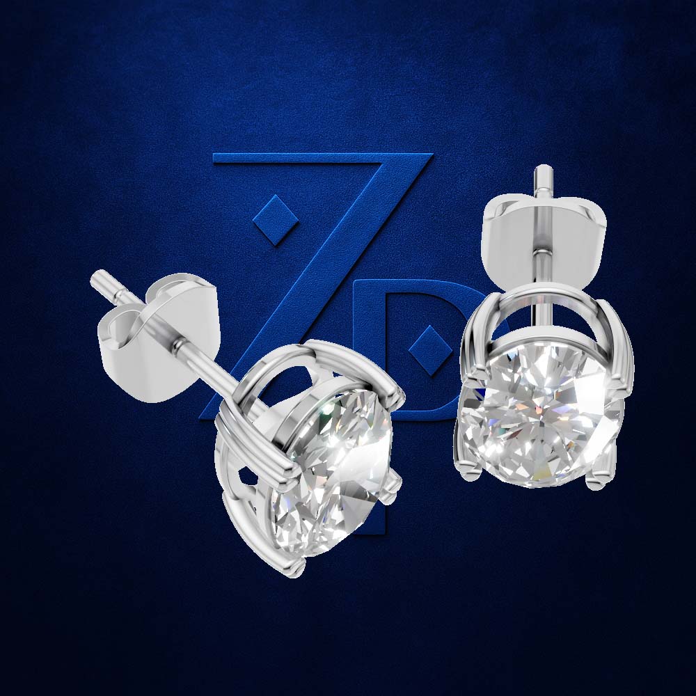 A pair of silver stud earrings with round clear gemstones in a prong setting, shown from two angles against a dark blue textured background with a faint stylized 'ZPD' logo.