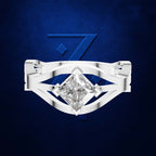 A silver-toned ring featuring a large, brilliant-cut clear gemstone in a prong setting, set against a textured dark blue background with a subtle stylized '7' design.