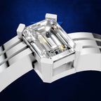 A close-up of a white metal ring band with a large rectangular emerald-cut clear gemstone, shown against a dark blue textured background.