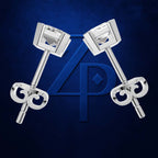 A pair of silver-toned stud earrings with square clear gemstones and decorative scroll-shaped backings, arranged symmetrically in front of a dark blue background with a large stylized blue 'AP' logo.