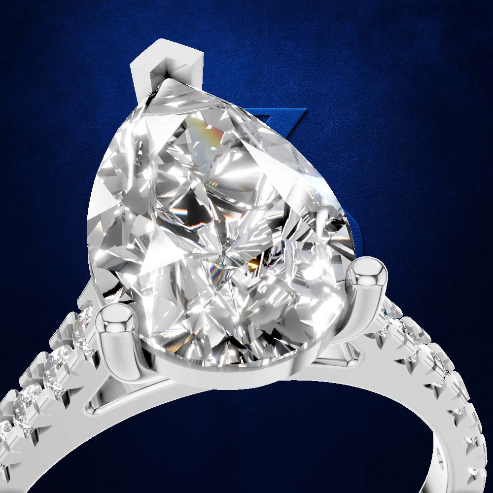 A close-up studio shot of a silver-toned ring with a large pear-cut clear gemstone in a prong setting, with smaller stones along the band, against a dark blue textured background.