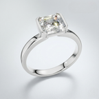 An emerald-cut diamond engagement ring in a polished white gold or platinum band, shown on a clean light gray background.
