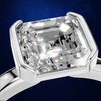 A close-up of a silver ring with a large cushion-cut clear gemstone in a prong setting, shown against a dark blue background.