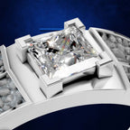 A close-up of a white gold or platinum ring featuring a large square princess-cut diamond in a four-prong setting, set against a dark blue textured background.
