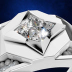 A close-up studio shot of a geometric silver ring featuring a princess-cut clear gemstone in a highly polished setting, set against a dark blue textured background.