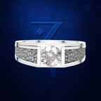 A silver-toned ring with a large round clear center stone and textured pavé side stones, shown against a dark blue textured background with a blue stylized '7' logo behind it.